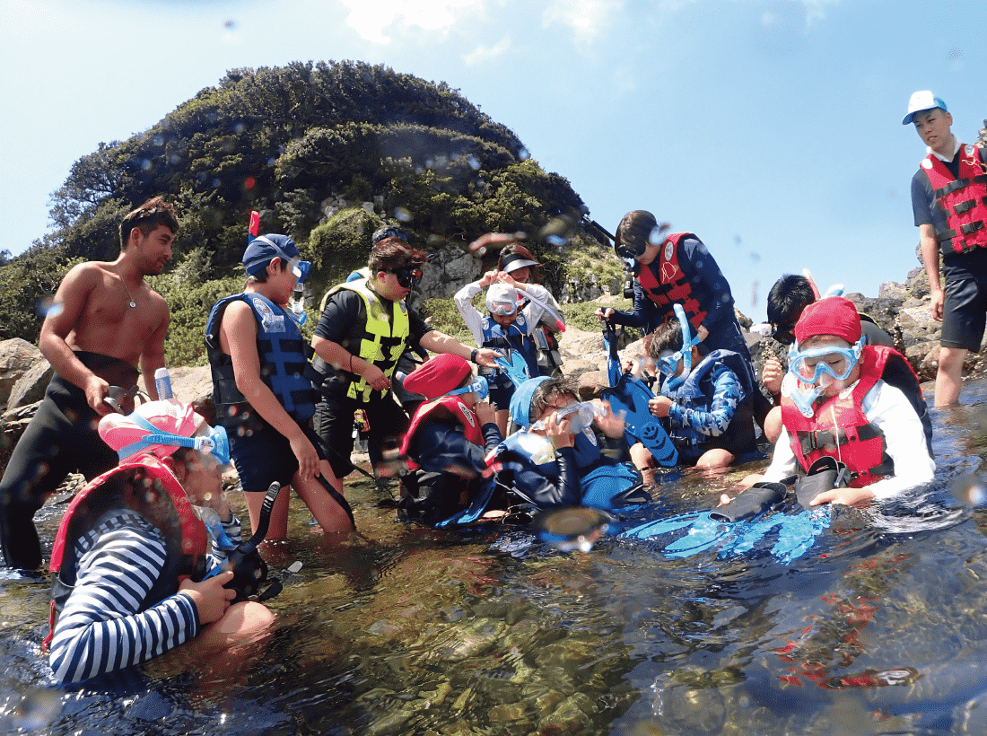 初めてのスノーケル体験を無人島で行った地元の小学生達が、浅い場所でみんなで固まって遊んでいる