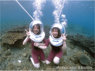 サンゴ群生を後ろに水中で記念撮影をする若い女性二人。