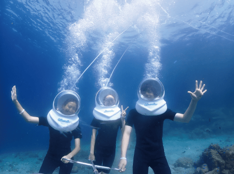 青く澄んだ日に体験した三名が、海の底を歩きながらこちらに手を振っている様子。